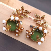 Gold and green earrings with leaf designs on a wooden surface
